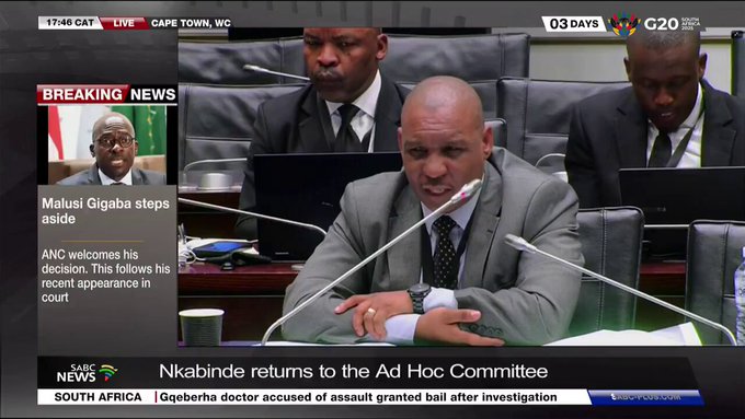 A screenshot of a live SABC News TV broadcast from Cape Town, showing a parliamentary committee room with several men in suits seated at a table, one speaking into a microphone; the screen includes news tickers and headlines about Nkabinde returning to the Ad Hoc Committee, alongside unrelated breaking news about Malusi Gigaba stepping aside and a doctor granted bail.