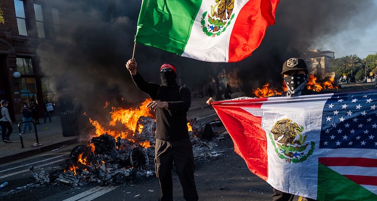 Commentary's tweet card. You’ve seen the image: A shirtless young man, wearing a mask and gloves, waves a Mexican flag while standing on the roof of a defaced car. He’s ringed by flames from a nearby burning vehicle....