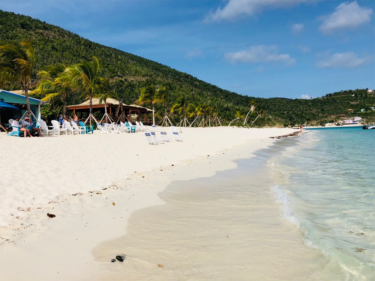 caribjournal's tweet card. You step off the boat and your toes are in the sand in seconds. Music is floating out of the bar. Someone hands you a Painkiller.