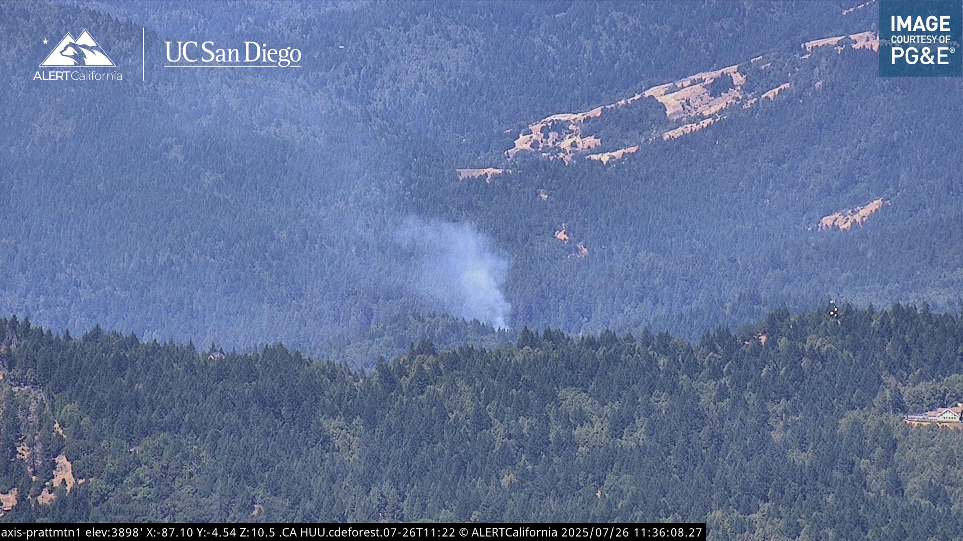 KymKemp's tweet card. The fire appears to be located in rugged terrain, making access difficult.