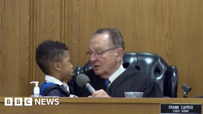 Judge Frank Caprio wearing a gown and sitting in court with a child next to him in the presiding chair