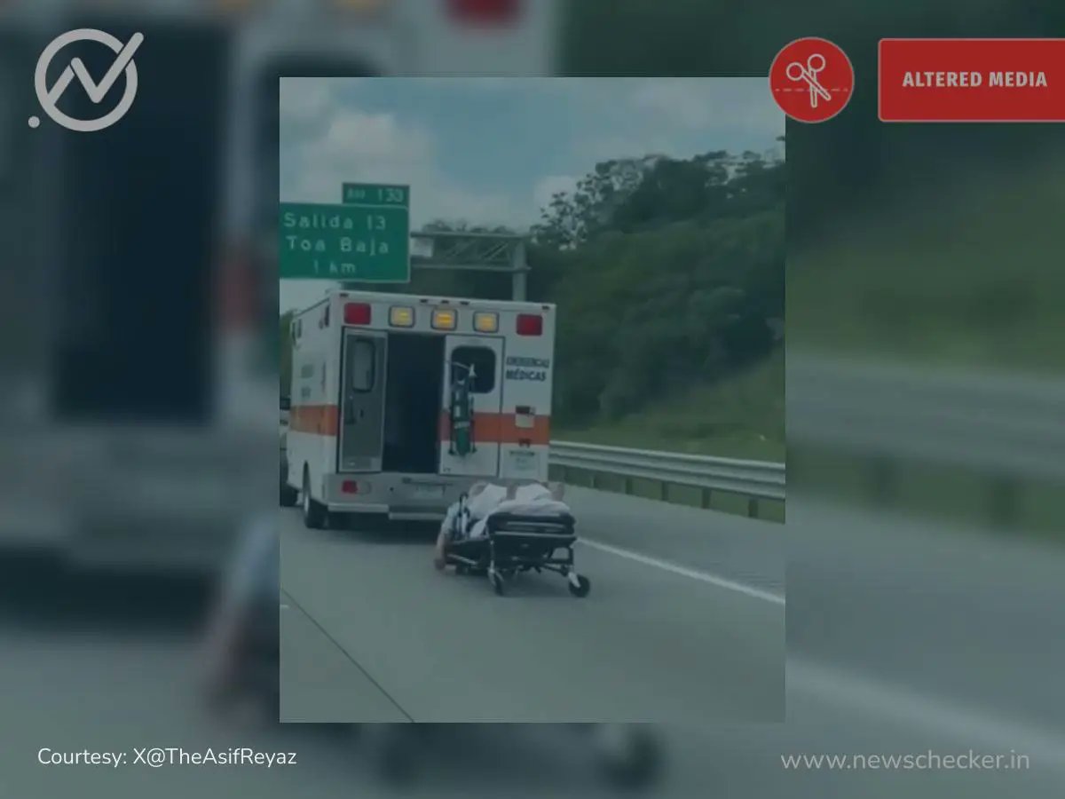 NewscheckerML's tweet card. തമിഴ്‌നാട്ടിലെ കൂനൂരിലെ ഒരു ഹൈവേയിൽ ആംബുലൻസിന്റെ വാതിൽ പെട്ടെന്ന് തുറക്കുകയും ഒരു രോഗിയോടൊപ്പം  സ്ട്രെച്ചർ റോഡിലേക്ക് ഉരുണ്ടു വീഴുകയും  ചെയ്യുന്ന