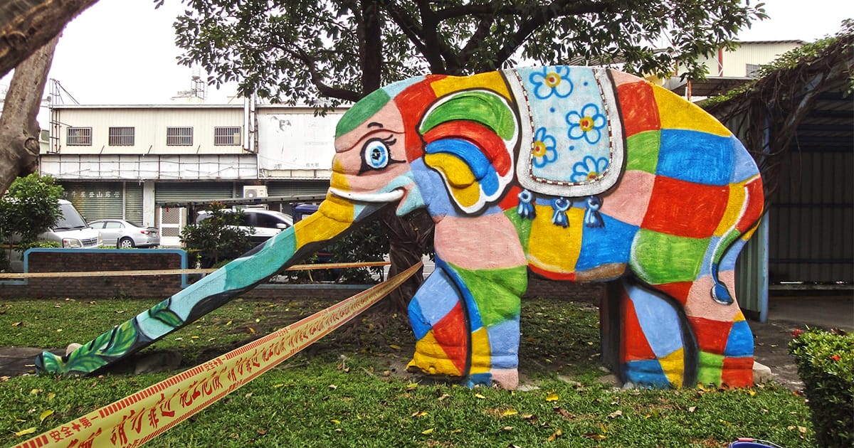 blogdockerfb's tweet card. Through the parks of Taiwan, a dwindling herd of vintage elephant slides trudge alongside ball courts and buildings.