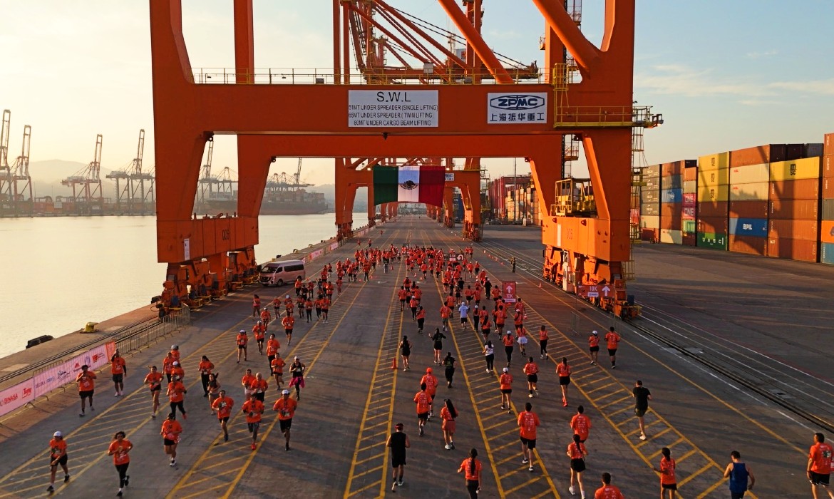 GrupoT21's tweet card. Bajo el primer sol del Pacífico, miles de corredores comenzaron a llenar el Parque Industrial Fondeport en Manzanillo. Eran las