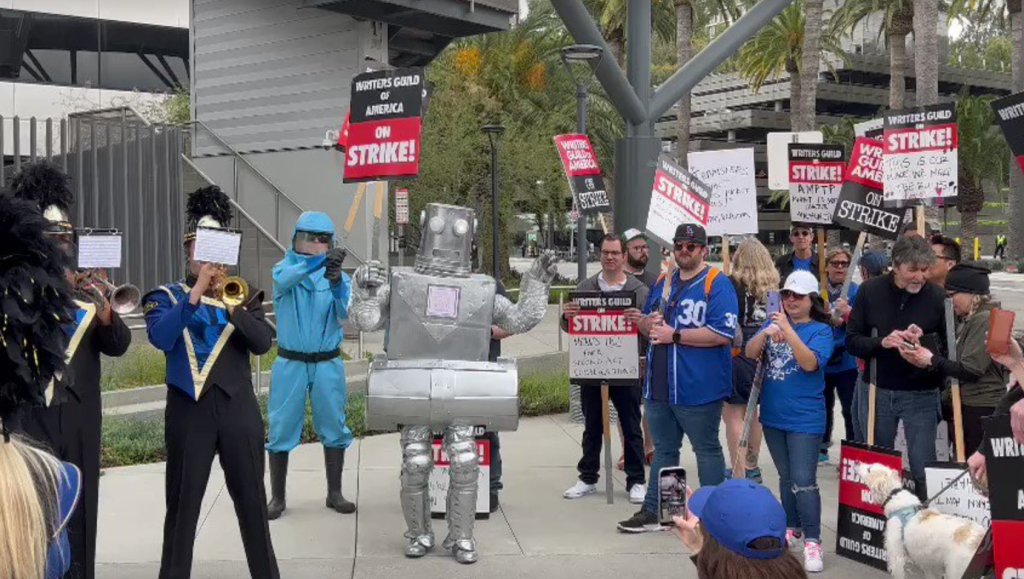 DEADLINE's tweet card. Sen. Gillibrand addresses a NY crowd; In L.A., Lil Wayne sends hamburgers, a robot marches & a marching band plays outside NBCU
