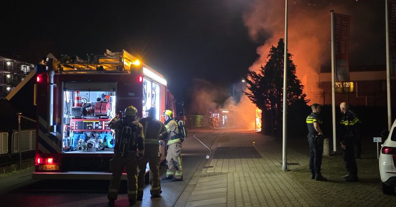 Heg in brand naast bedrijfspand; brandweer schaalt op