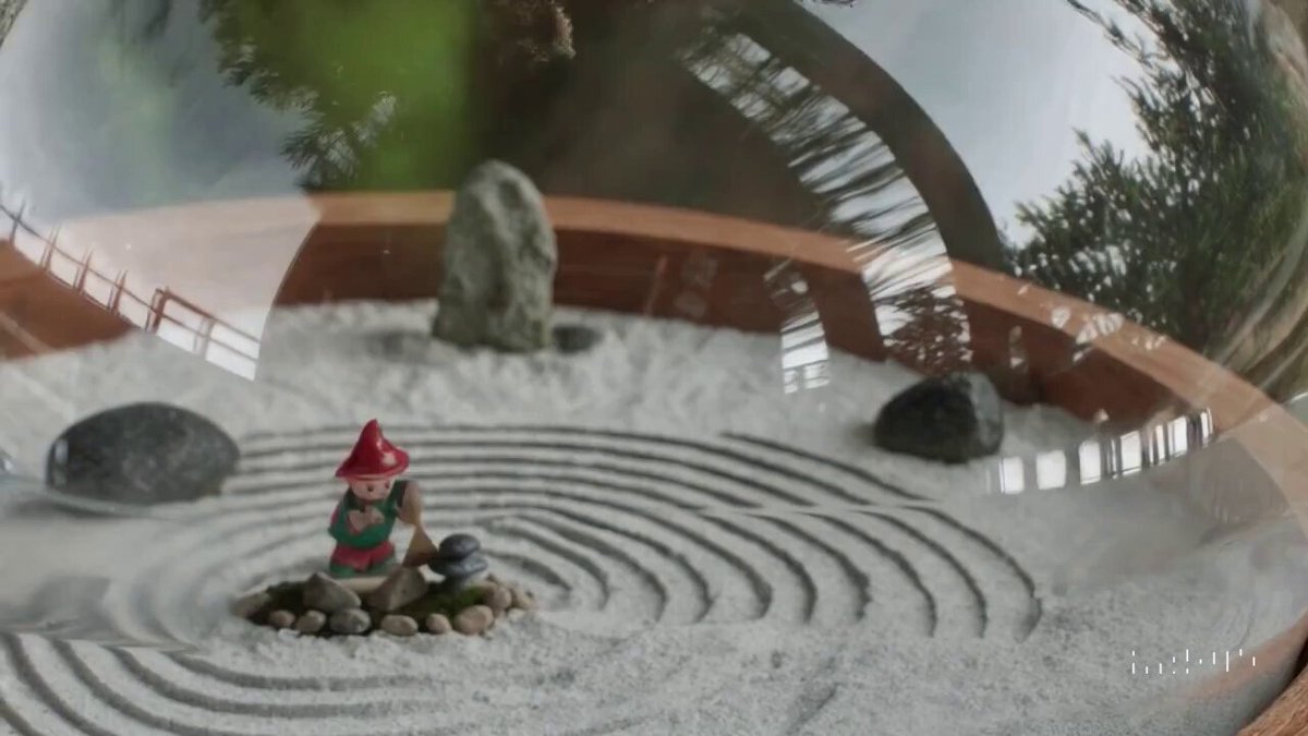 A close up view of a glass sphere that has a zen garden within it. There is a small dwarf in the sphere who is raking the zen garden and creating patterns in the sand.