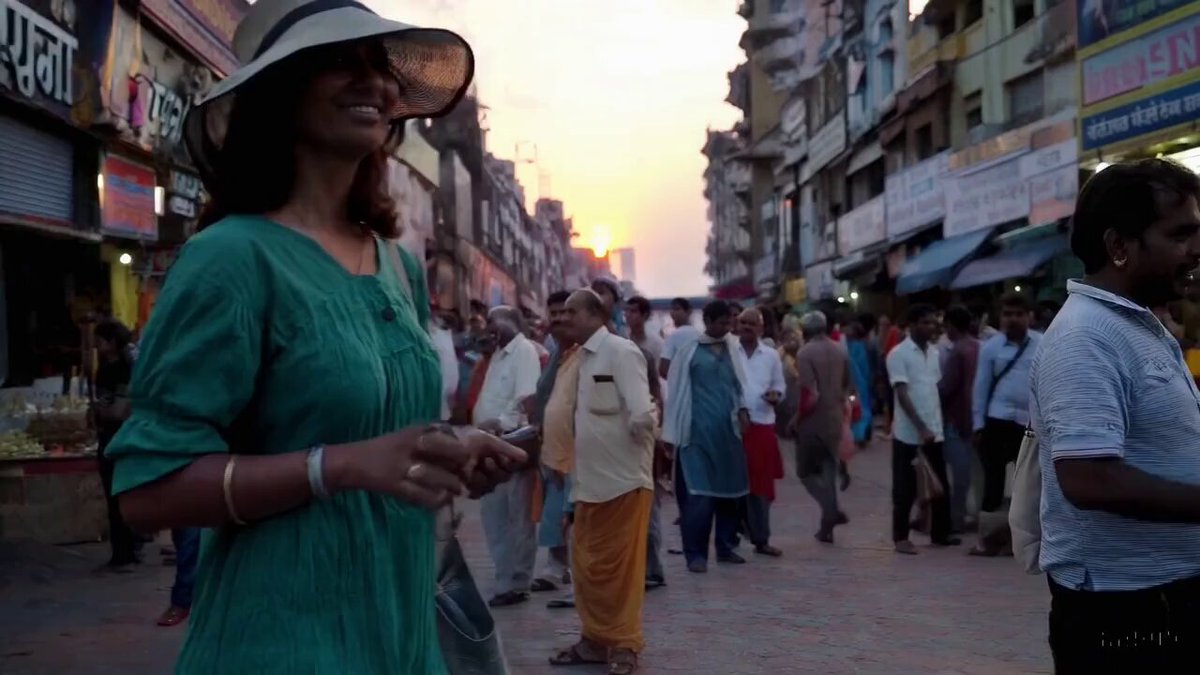 a woman wearing a green dress and a sun hat taking a pleasant stroll in Mumbai, India during a beautiful sunset.
