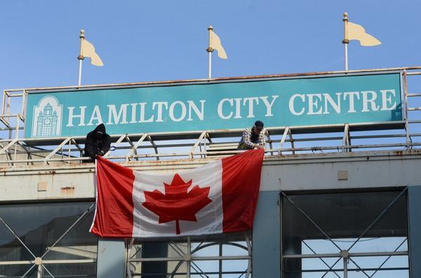 Workers hang a Canadian flag above York Blvd in Hamilton in preparation for Tuesday's funeral for Cpl Cirillo #HamOnt