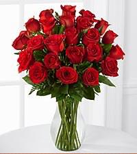 -sets a vase of red roses on the kitchen table with a box of chocolate beside it and a wrapped gift box next to it-