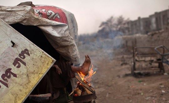 Evsiz bir adam yaktığı cılız ateş ile ayaklarını ısıtmaya çalışıyor. | Kabil, Afganistan, 2011