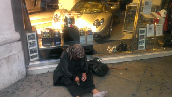 bmomark's tweet image. A disabled homeless woman sits outside a showroom housing a Zonda and a Veyron         #economicspectrum