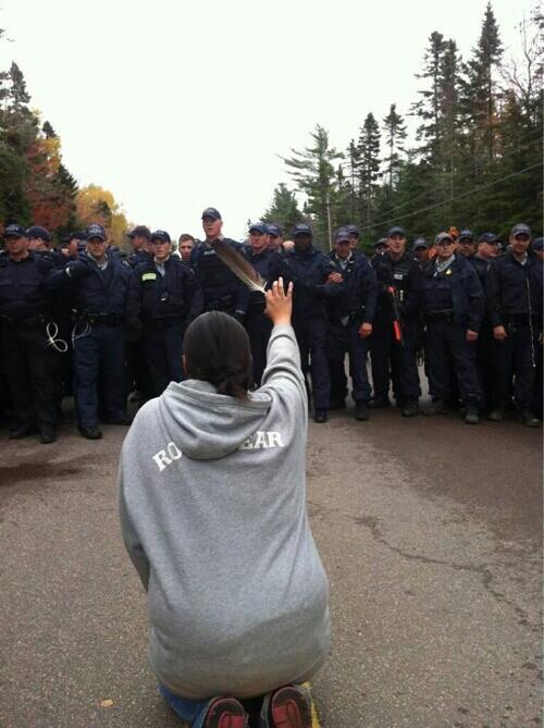 Haunting Photo Cda now Via @APTNNews 1 peaceful protestor holdsup eagle feather to wall of RCMP #rexton #elispogtog