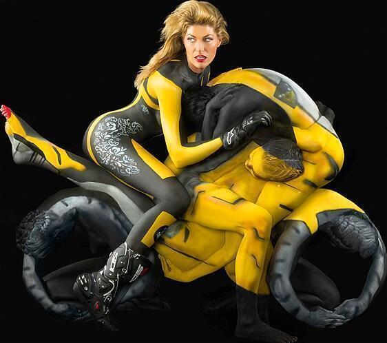 Una mujer monta una moto deportiva compuesta por varios modelos desnudos cubiertos de pintura corporal.