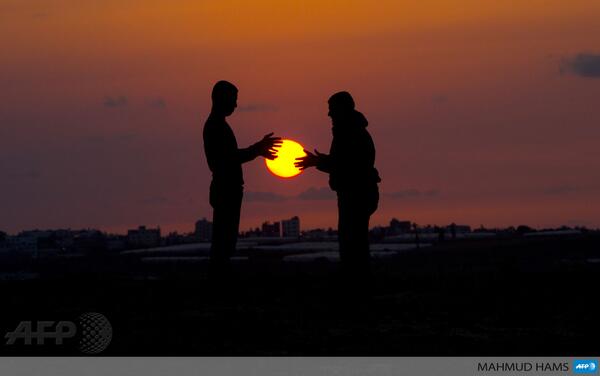 afpfr's tweet photo. Deux jeunes hommes jouent avec le soleil couchant à Beit Hanoun (nord de la bande de Gaza) http://t.co/DgyF49wNzh #AFP [via @sbeaugeAFP]