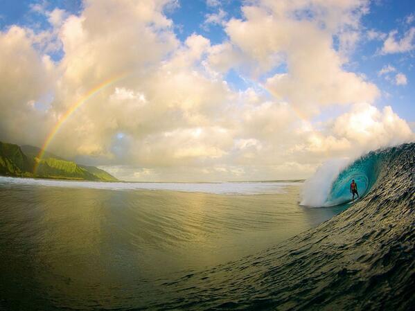 Surfer rides the perfect wave as an astonishing rainbow breaks out around him, Tahiti.