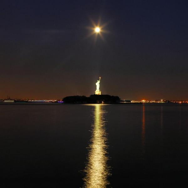 GaryHershorn's tweet photo. The full moon reflects off the water behind the Statue of Liberty in New York #newyork #newyorkcity @nyc #supermoon http://t.co/dbMtow5JKD