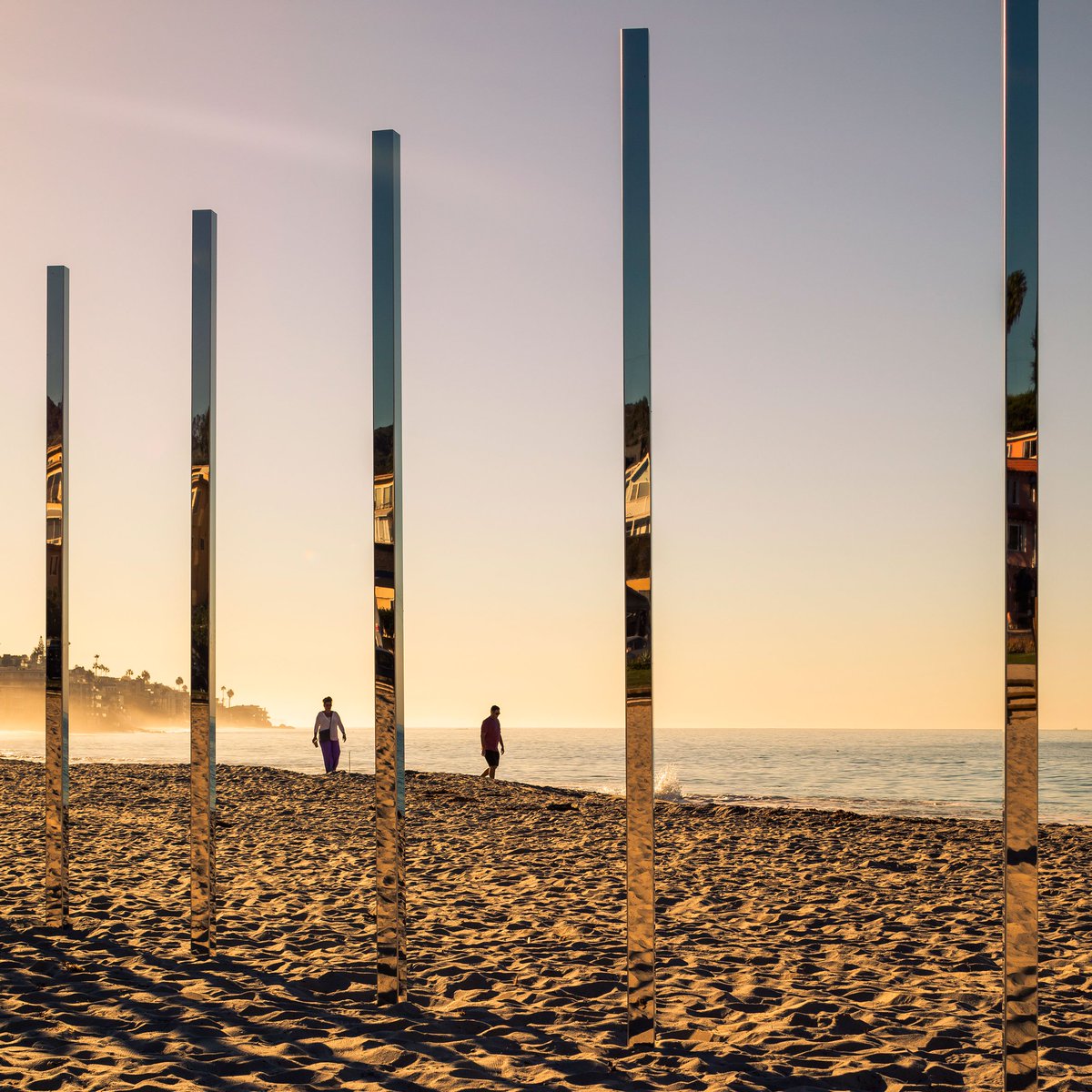 dezeen's tweet photo. An arc of mirrored posts installed by American artist Phillip K Smith III reflects sea and sky at Laguna Beach: https://t.co/pP6FXJbrsF https://t.co/GTaDfHZXlF