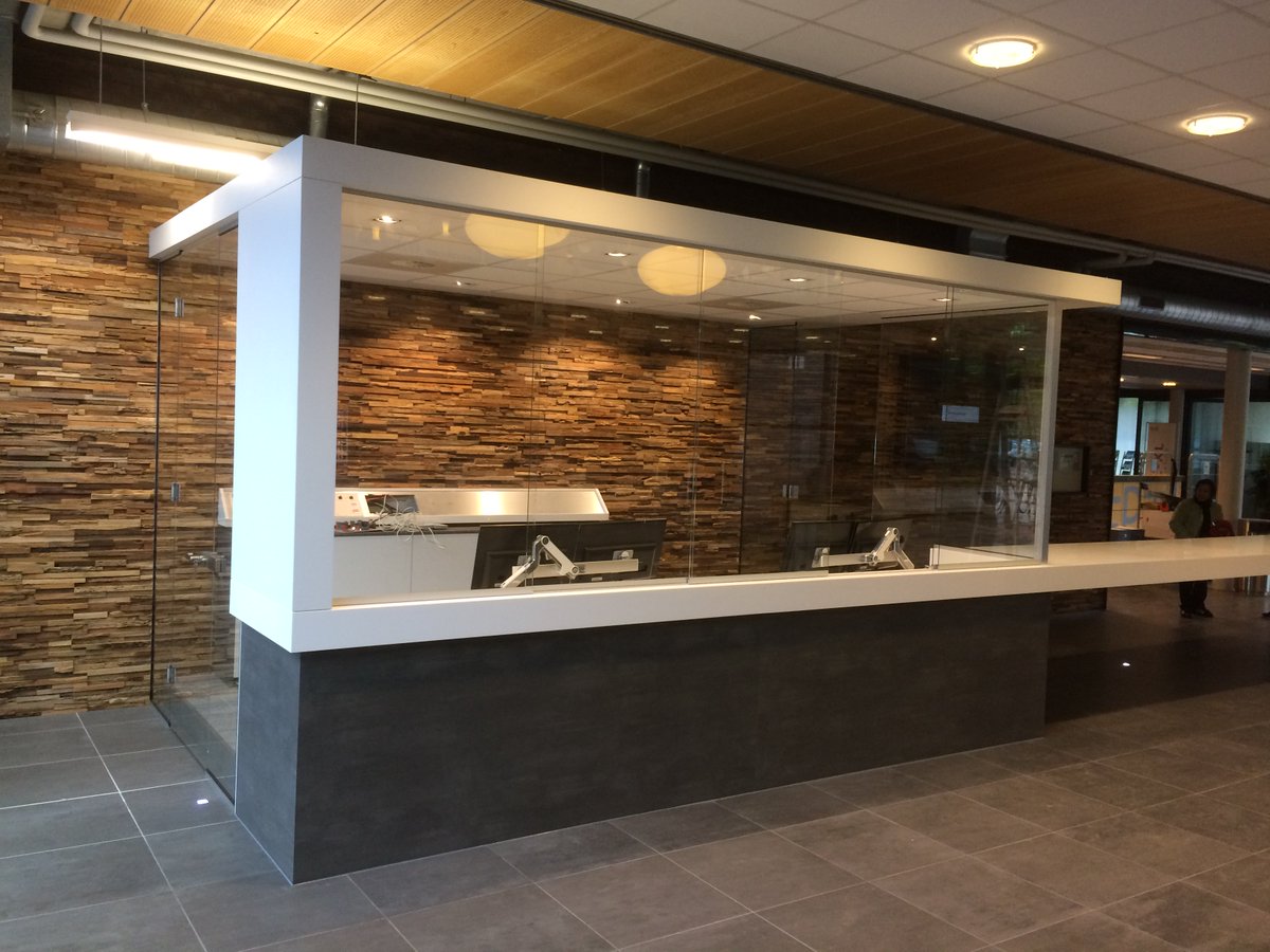 Een receptie volledig afgesloten met glas. Schuifdeuren voor de balie en een deur aan de zijkant.