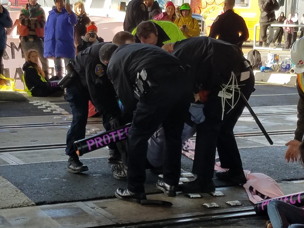 Indybay's tweet photo. Police have wrestled a few protesters from lockboxes, then pauses on arrests..
#J20 #120Hours #ReclaimMLK #Ungovernable
. https://t.co/PGB389L7cA
