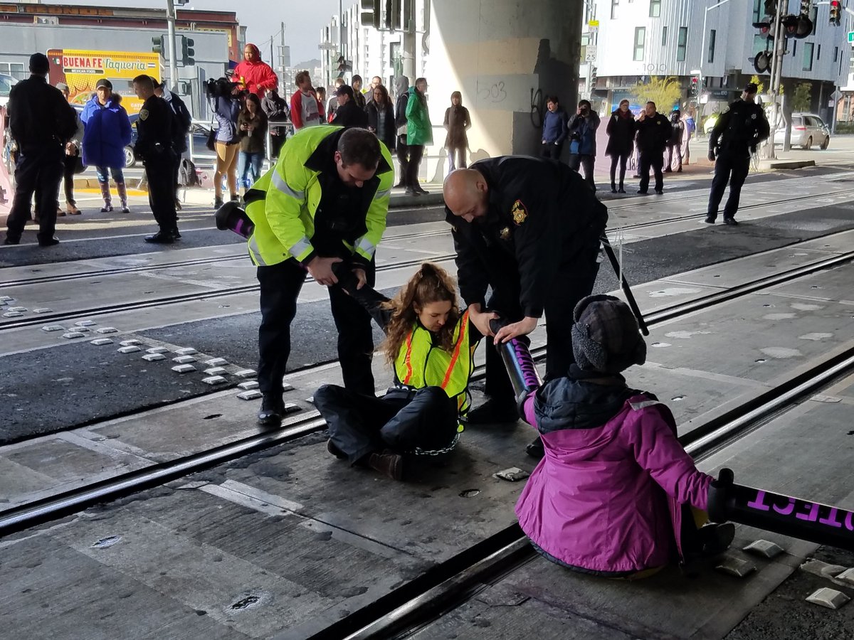 Indybay's tweet photo. After one protester is arrested, another runs in and locks down to take her place.
#J20 #120Hours #ReclaimMLK #Ungovernable https://t.co/c0rTD4XbVh