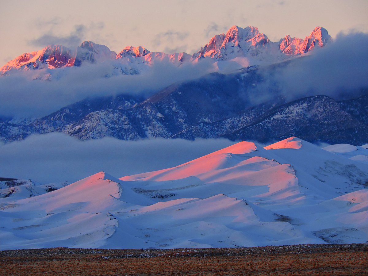 Snowy mountains glow pink as they appear through the clouds