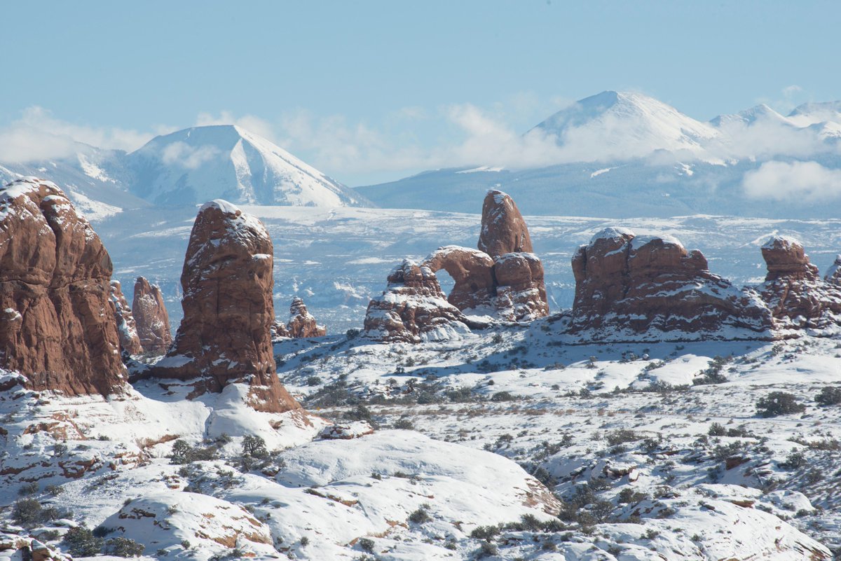 Snow covered arches and pinnacles in red sandstone, with snowy mountains in the background