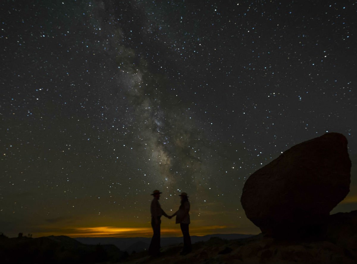 Two people wearing hats hold hands under a starry sky.