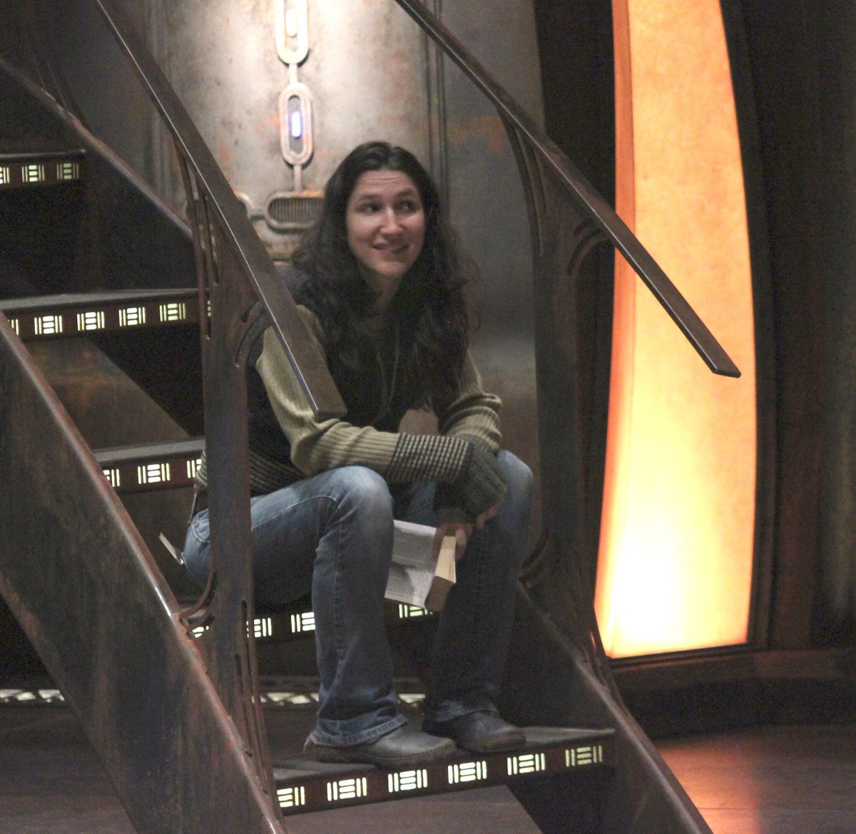 Woman sitting on staircase of a science fiction TV show set.