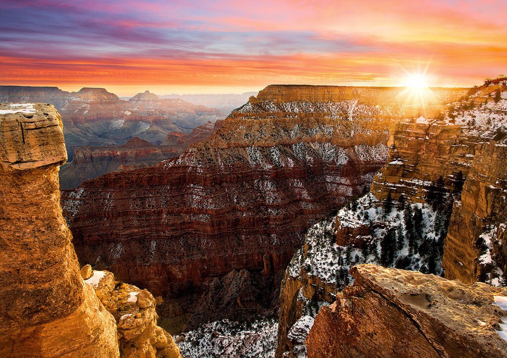 Sun appears over the rim of a snowy Grand Canyon