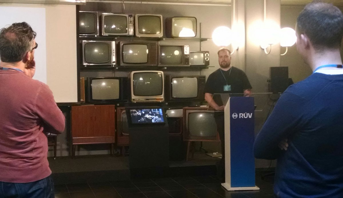 A man giving a talk in front of old televisions