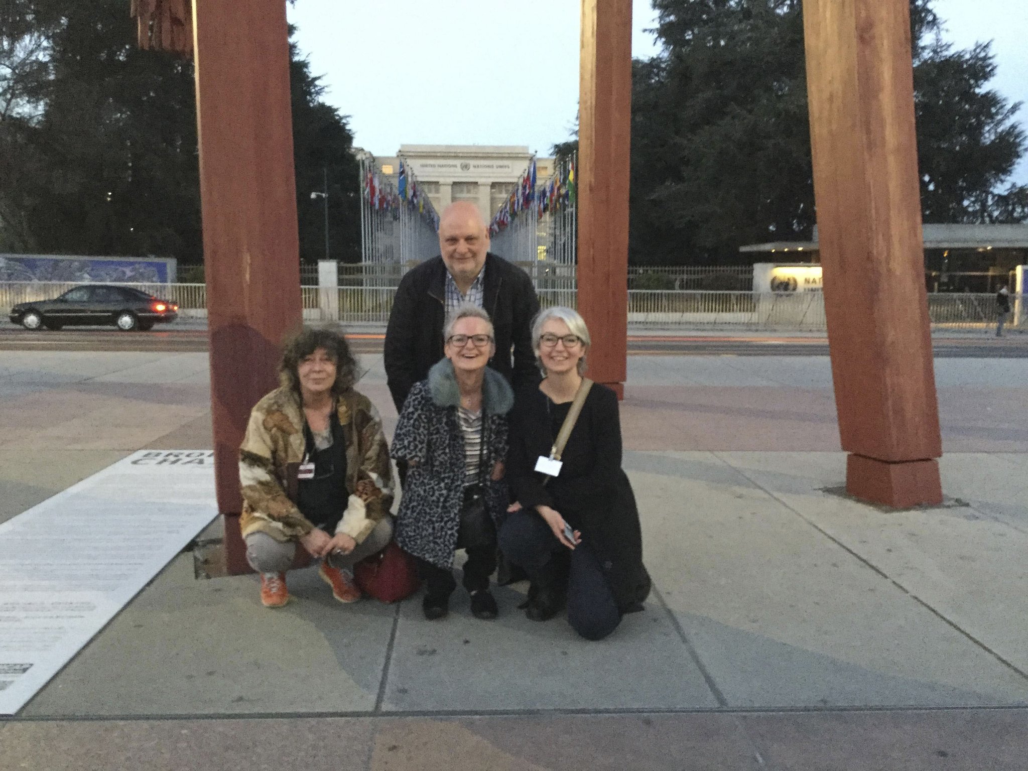 4 people in front of the UN building, 3 white women with white man at the back. They are crouching. 