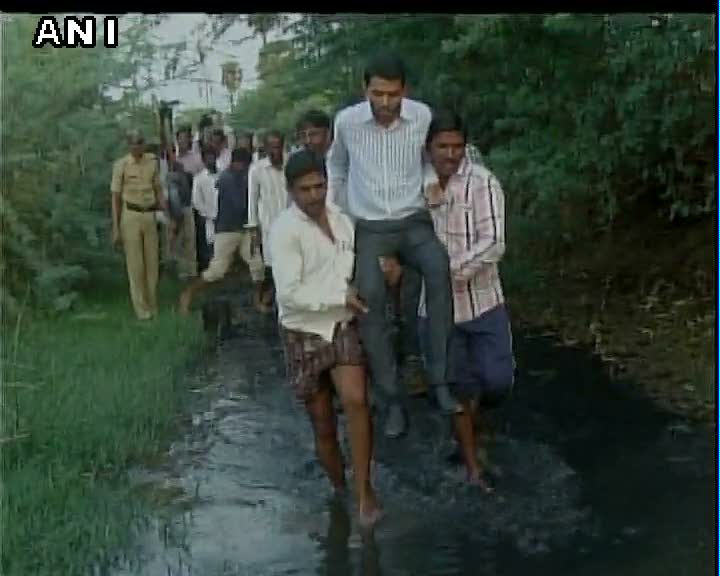Kurma Roa, CEO Zila Panchayat crosses a drain with help from locals, in Raichur, Karnataka.