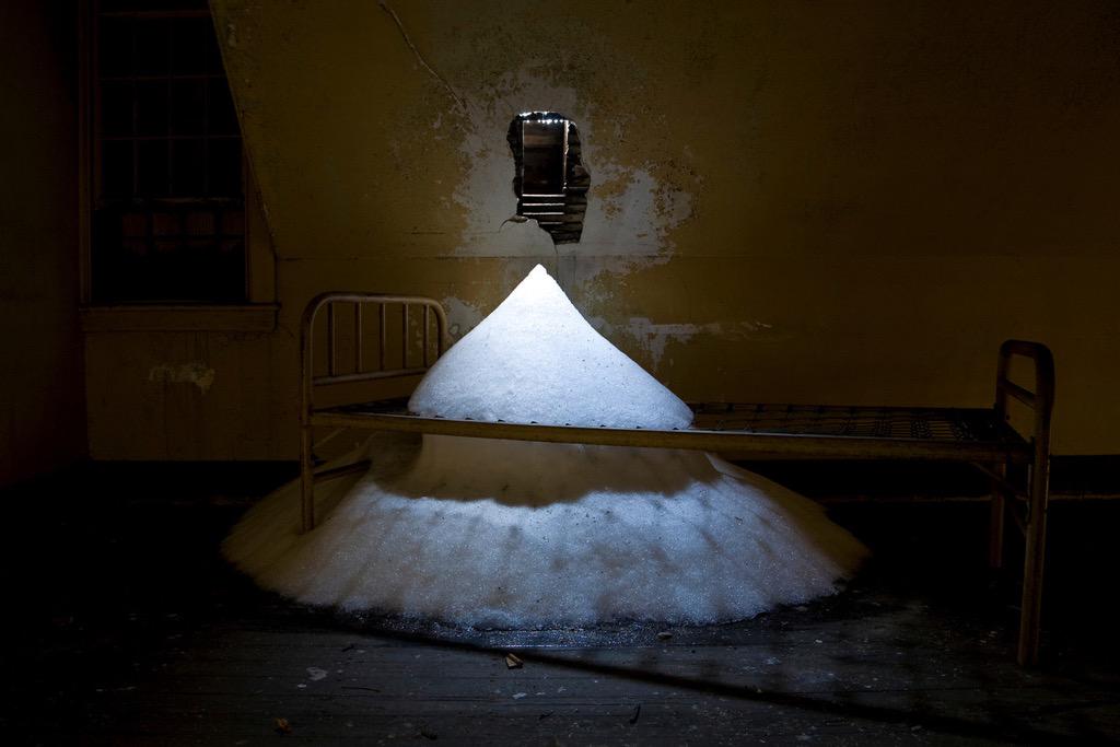 A Small hole in the ceiling allowed snow to pile up on a patient's bed frame at an Abandoned Asylum.