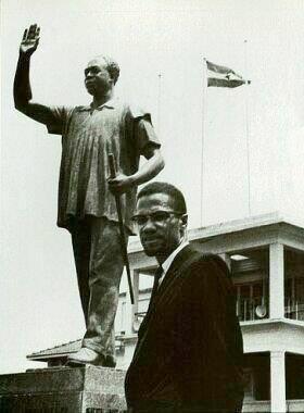 Malcolm X posing beside a statue of Dr. Kwame Nkrumah in Accra, Ghana. 1964.