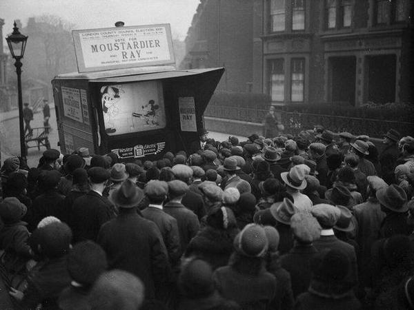 1931- Londoners flock to a mobile screen showing the latest Mickey Mouse film.