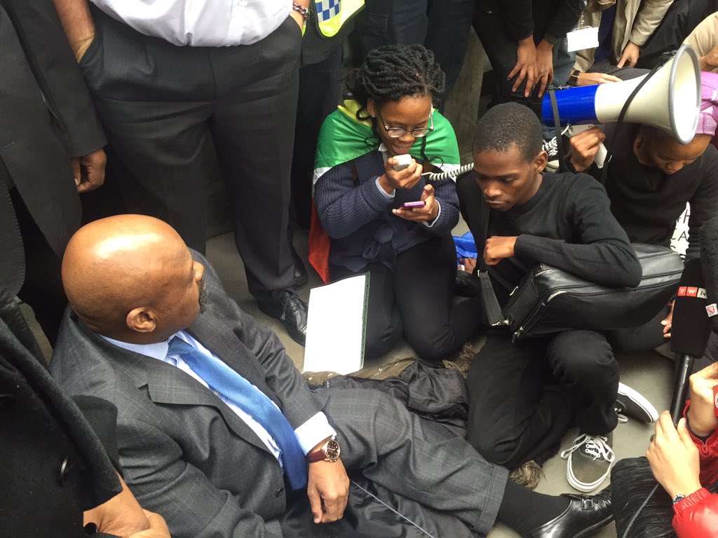 VumaniMkhize's tweet photo. SA High Commissioner Obed Mlaba was made to sit on the floor by #FeesMustFall campaigners here in London. https://t.co/x4buiOg2Ft