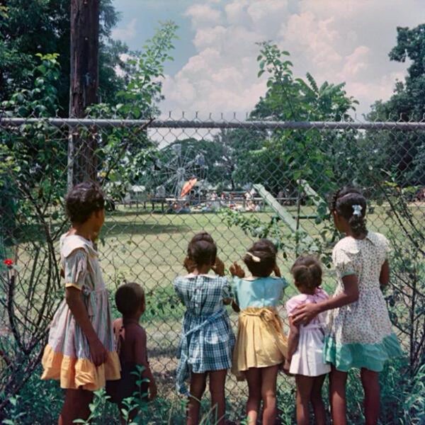 Black children watching as white children play in a whites only park, 1956.