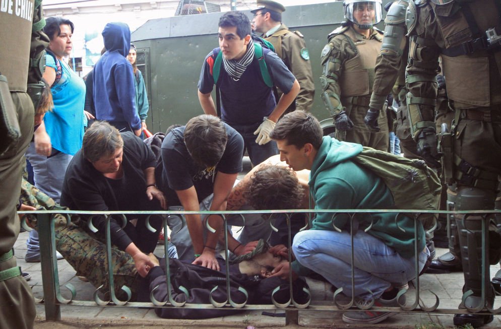 Chilean communist militants aid a student who had been shot at a protest as police stand by, he died hours later.