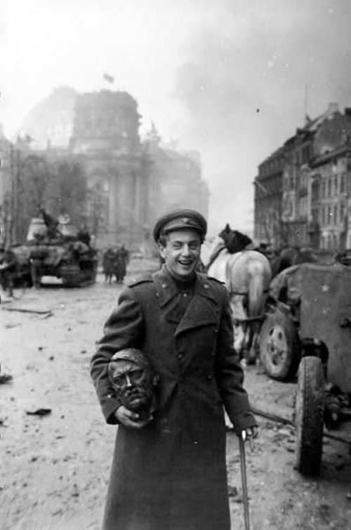 a Russian soldier carries a statue head of Nazi leader Adolf Hitler (May 1945)