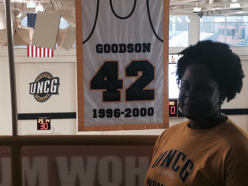 CoachABSS's tweet image. GHS's own Coach Goodson poses next to HER retired jersey at UNCG #shedidthat #division1athlete