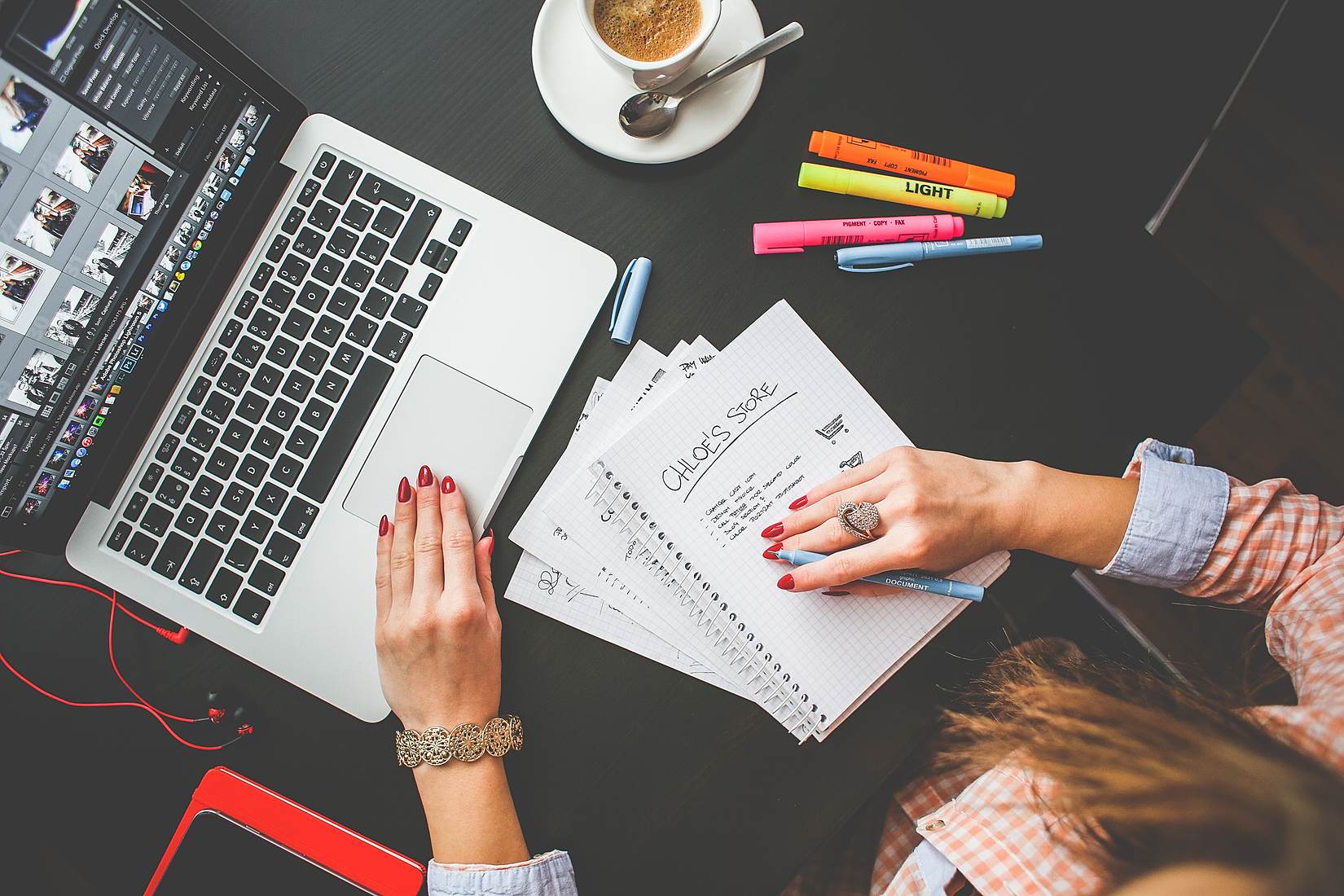  A person uses a laptop and a notebook while working on a freelance image editing project.