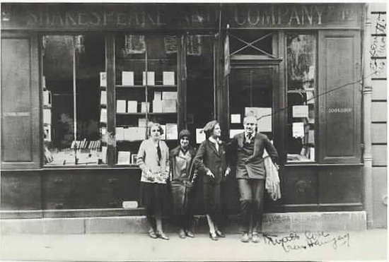 Four people pose in front of shop window displaying books.