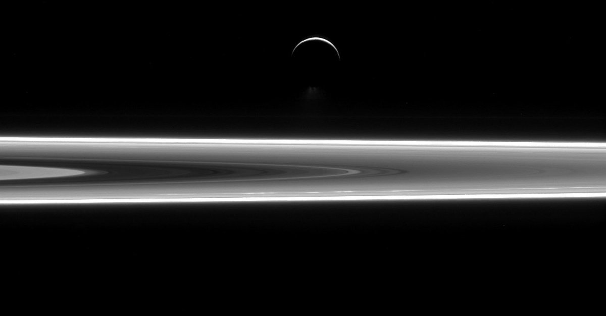 A thin crescent Enceladus floating above a sliver of Saturn's rings against darkness.