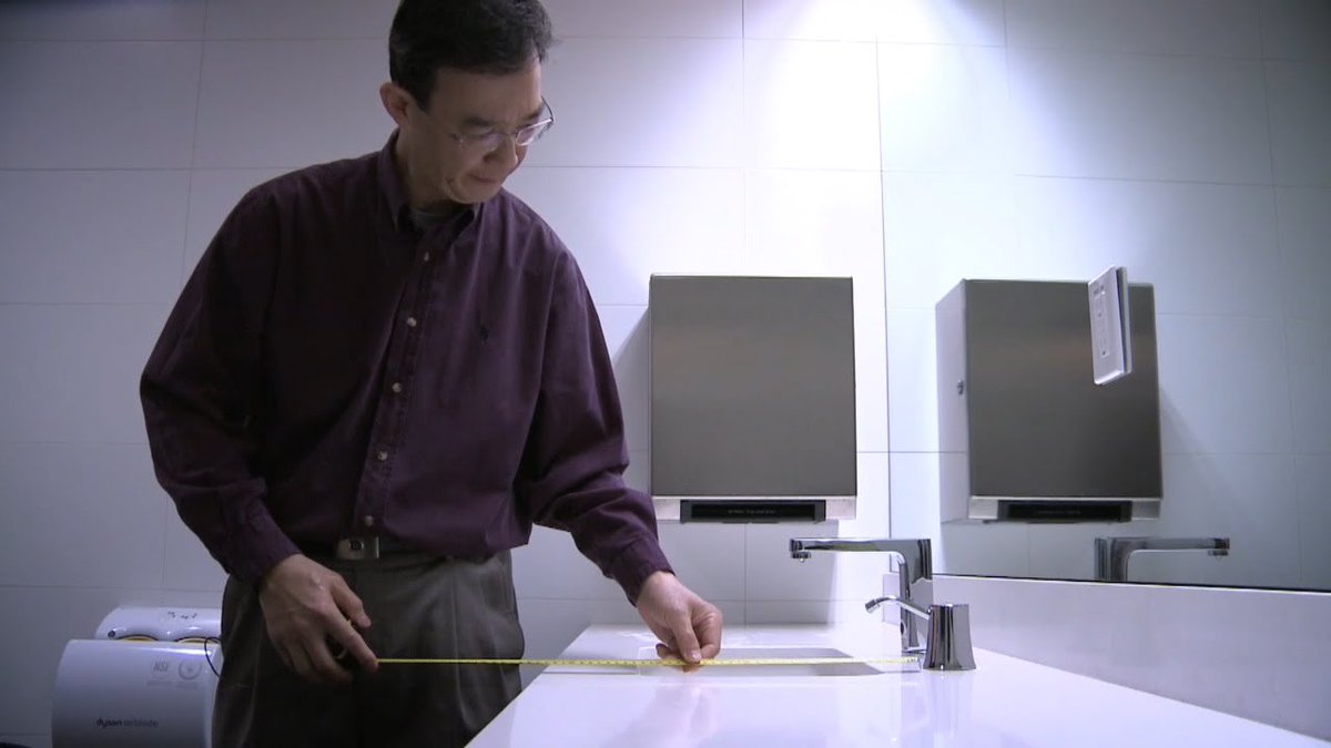 A trained accessibility assessor measures a newly built bathroom sink in a public venue for accessibility requirements.