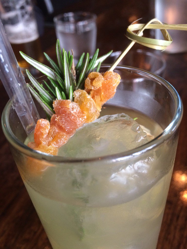 A cocktail with sprigs of rosemary and clumps of skewered ginger