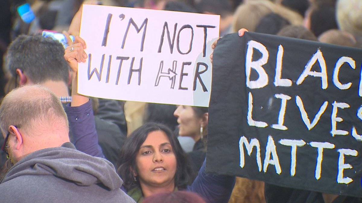 TLinNEWS's tweet photo. Spotted at #Hillary rally at Rainier Beach HS.  @cmkshama holding sign expressing disapproval.  #komonews https://t.co/AwiSDsFvh1