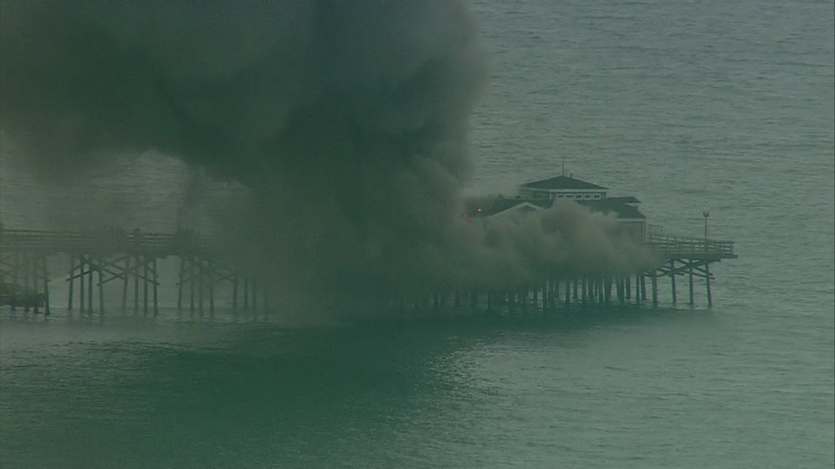 FOXLA's tweet photo. #BREAKING: Fire at former Ruby's Diner site at end of Seal Beach Pier. Flames and thick black smoke coming from roof https://t.co/1iyxnwcXVf