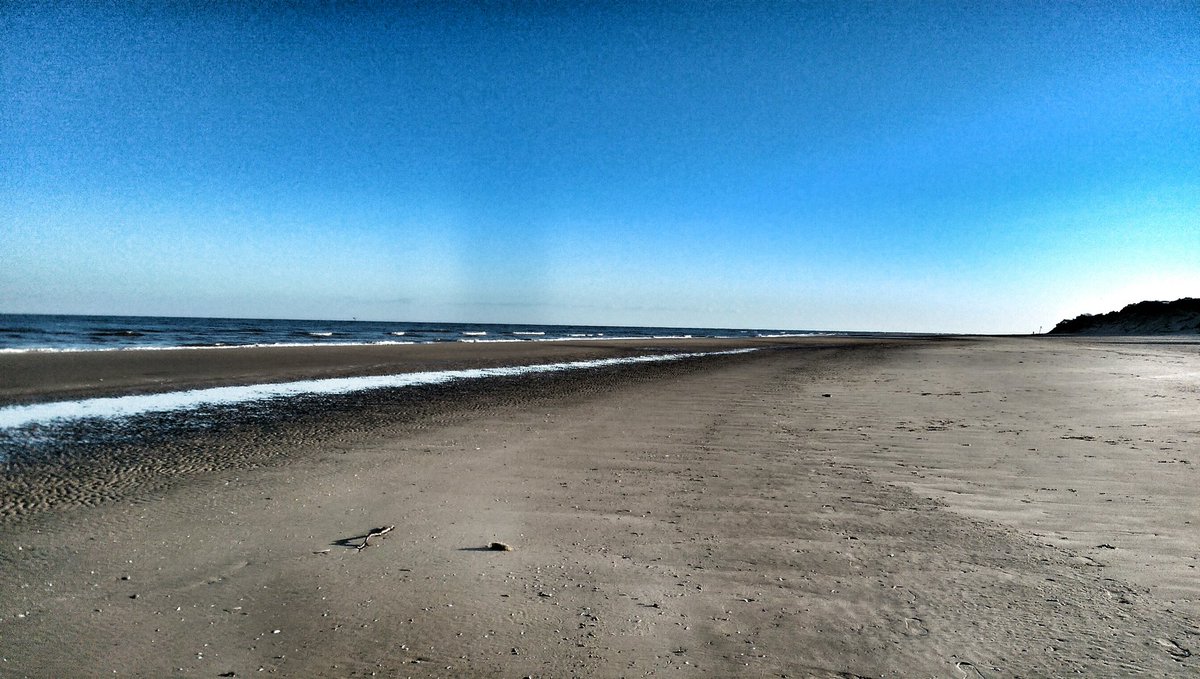 Clear, empty beach with clear blue skies, and sea on horizon.