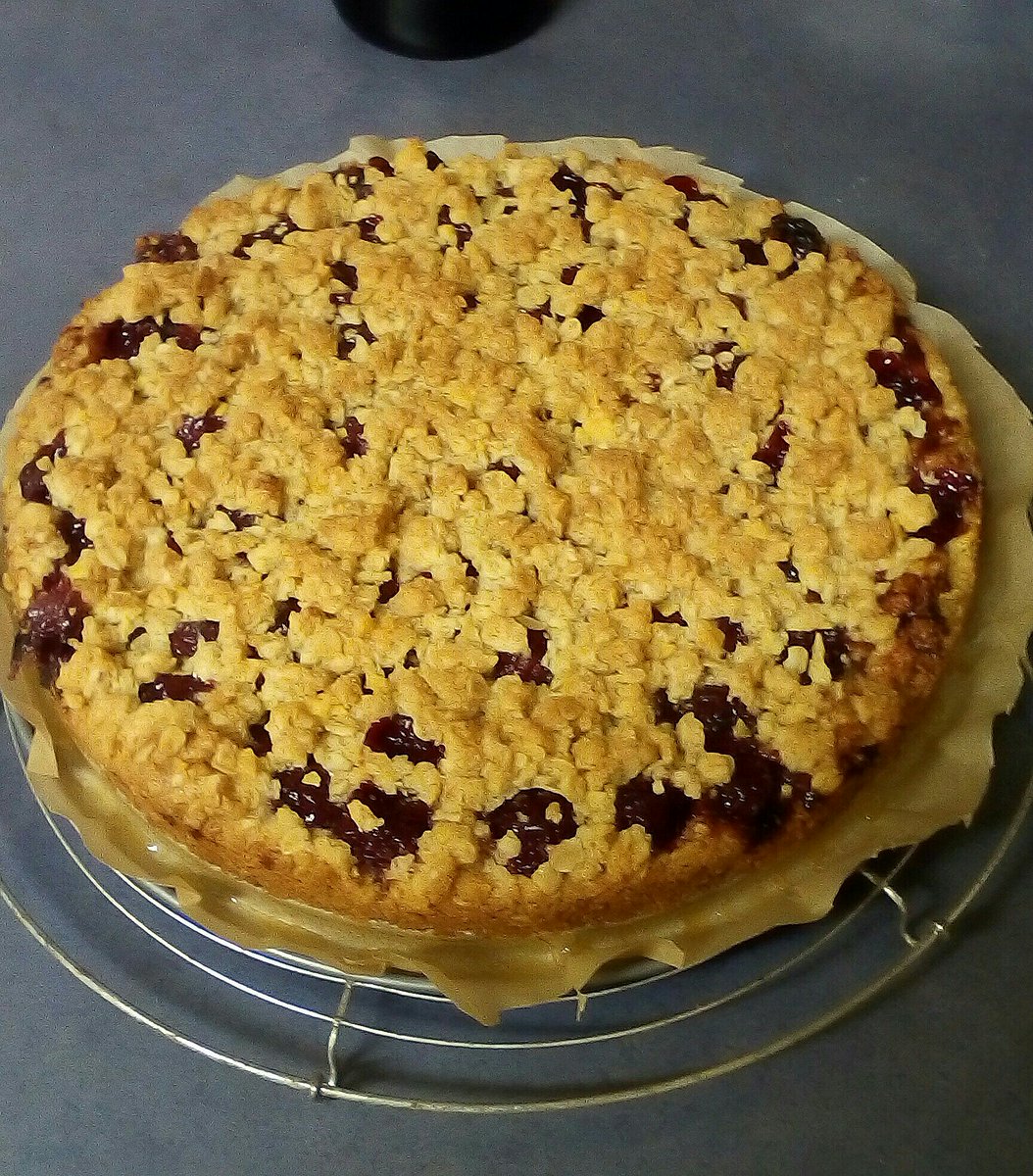 a cake with a cherry filling and golden brown crumble on top on a cooling rack.